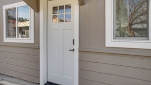 Una puerta blanca con un panel de vidrio, revestimiento color beige y una ventana con vista a árboles.