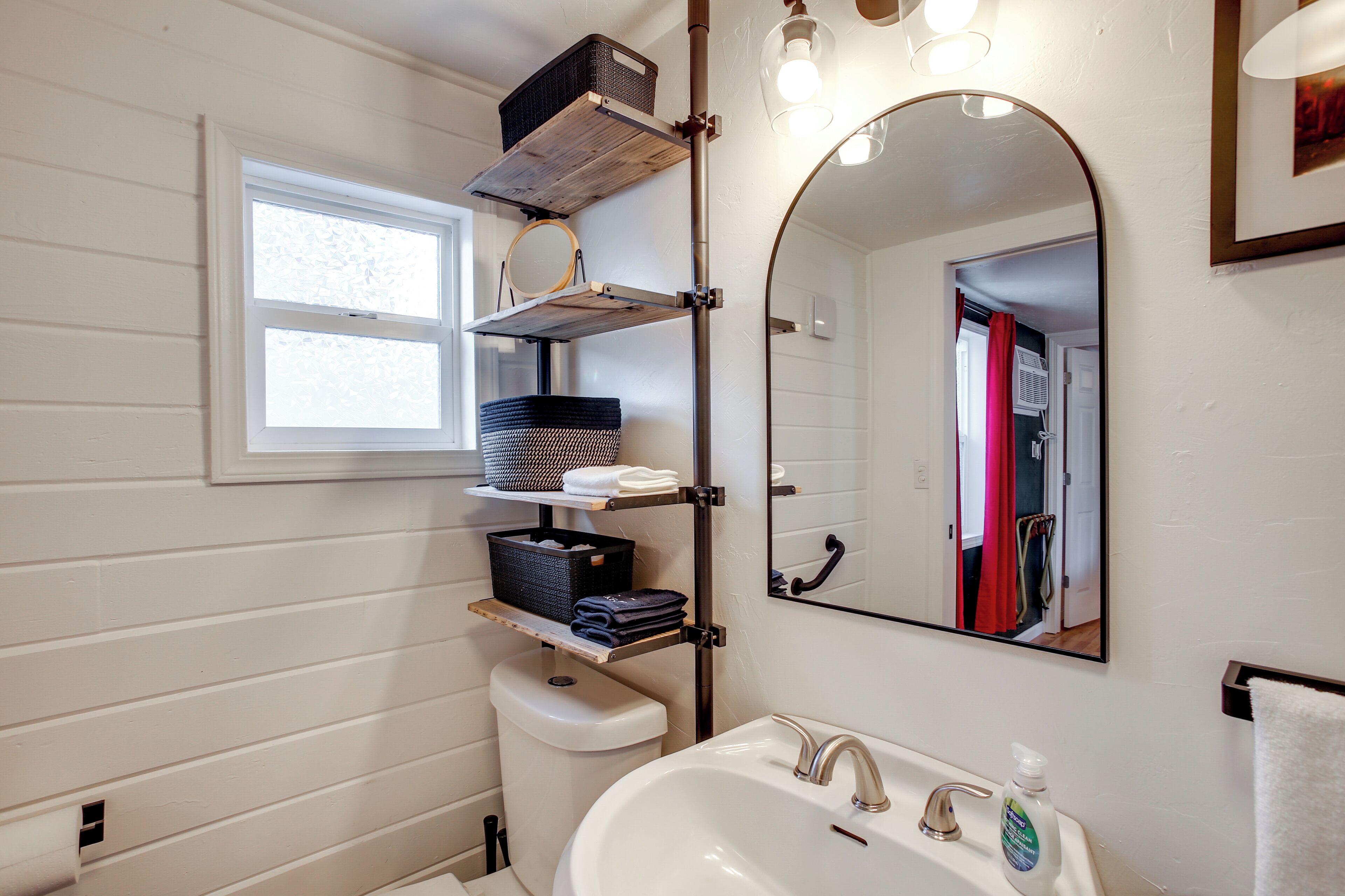 Une salle de bain avec un lavabo blanc, un miroir et des étagères où sont rangées des serviettes et des paniers.