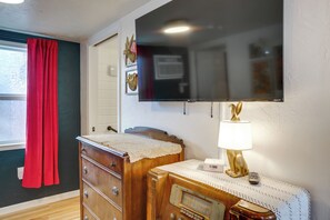 Habitació amb un aparador de fusta, un aparell de ràdio antic, una televisió penjada a la paret i una finestra amb cortines vermelles.