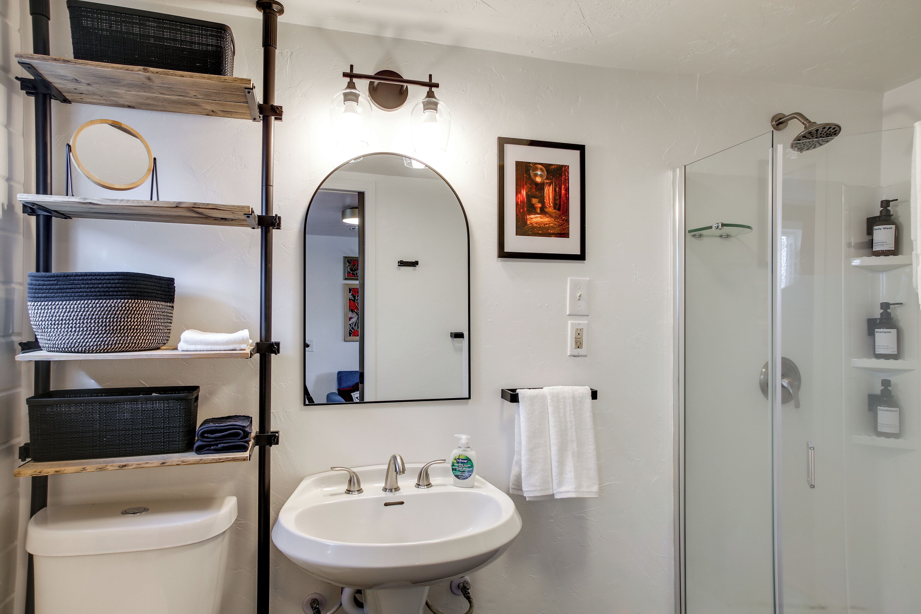 A bathroom with a white sink, a mirror, a framed picture, and a glass shower enclosure.