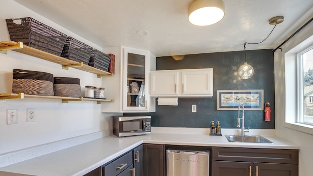 A compact kitchen with a microwave, sink, and stainless steel refrigerator. There are shelves with baskets and a window providing natural light. - Unit 2: Cozy 1-br, 3 Mi to Riverfront Park (Spokane)