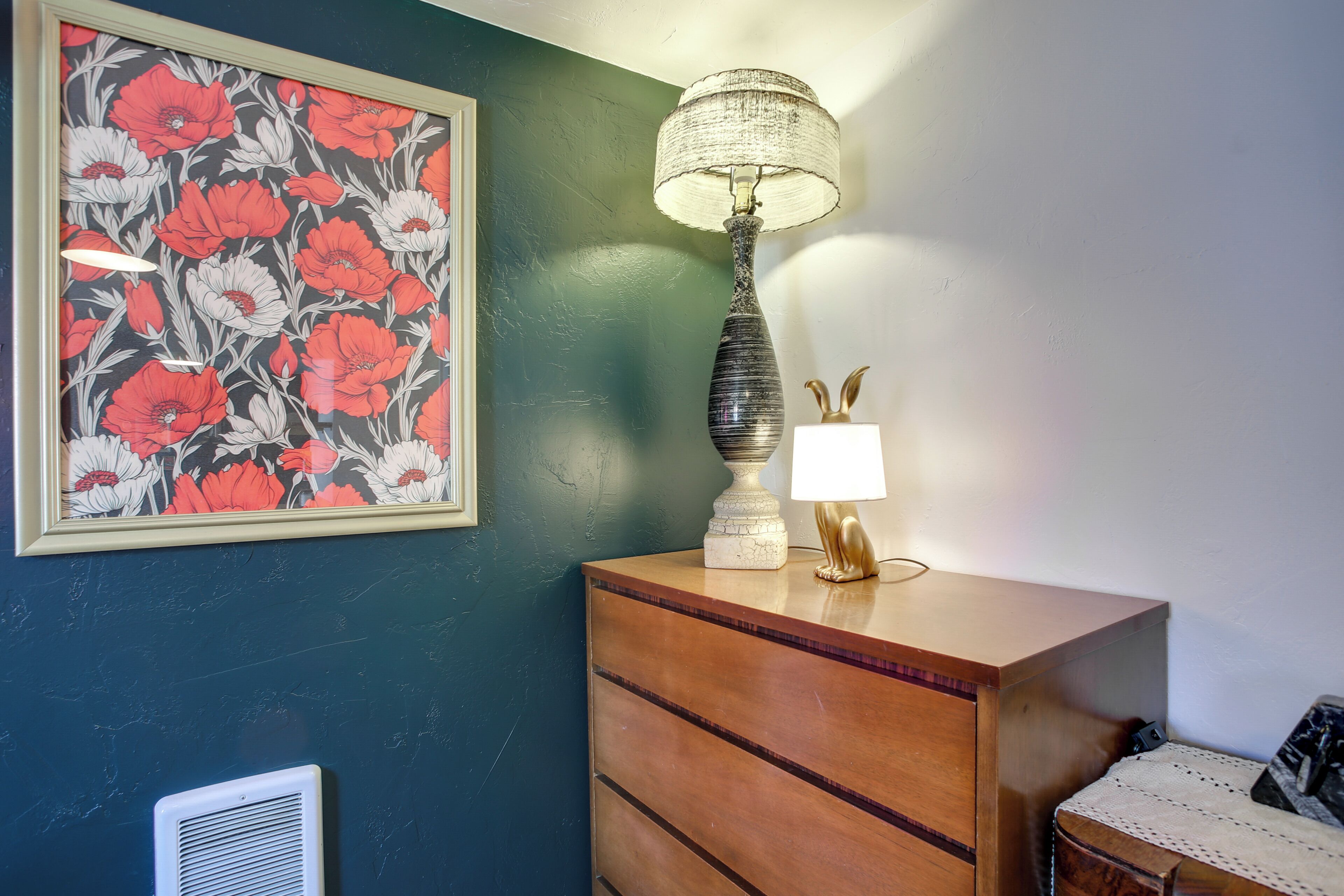 A room with a dresser, a lamp, a framed floral artwork, and a radiator.