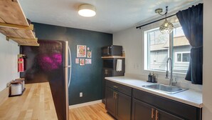 A kitchen with dark cabinets, a wooden countertop, a refrigerator, a microwave, a sink, and a window with curtains. - Unit 5: 1-br w/ Workspace, Quick Hospital Run (Spokane)