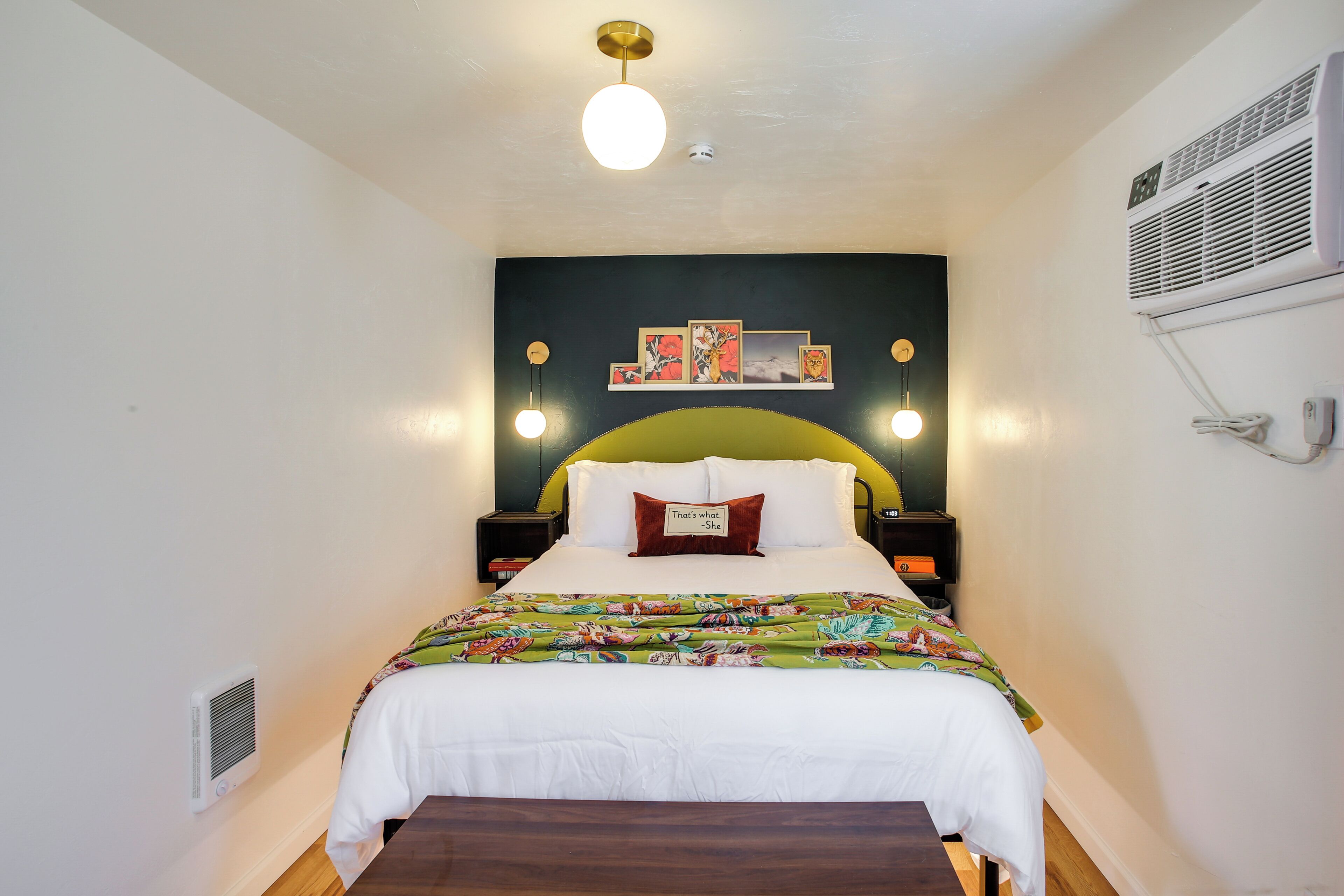 Une chambre à coucher comprenant un lit, des tables de chevet, un climatiseur fixé au mur et un luminaire au plafond.