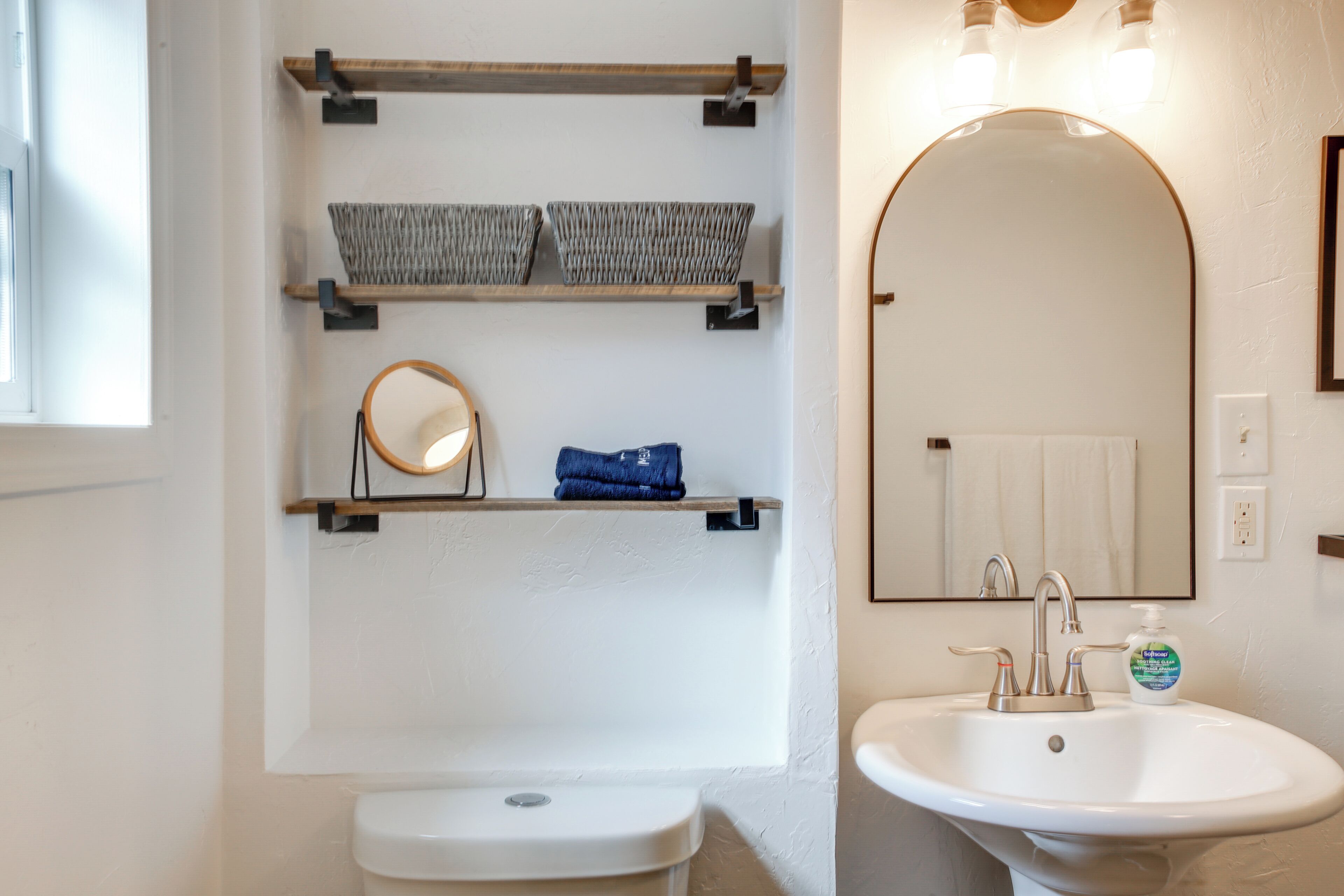 Een badkamer met toilet, wastafel, spiegel en planken met manden en een handdoek.