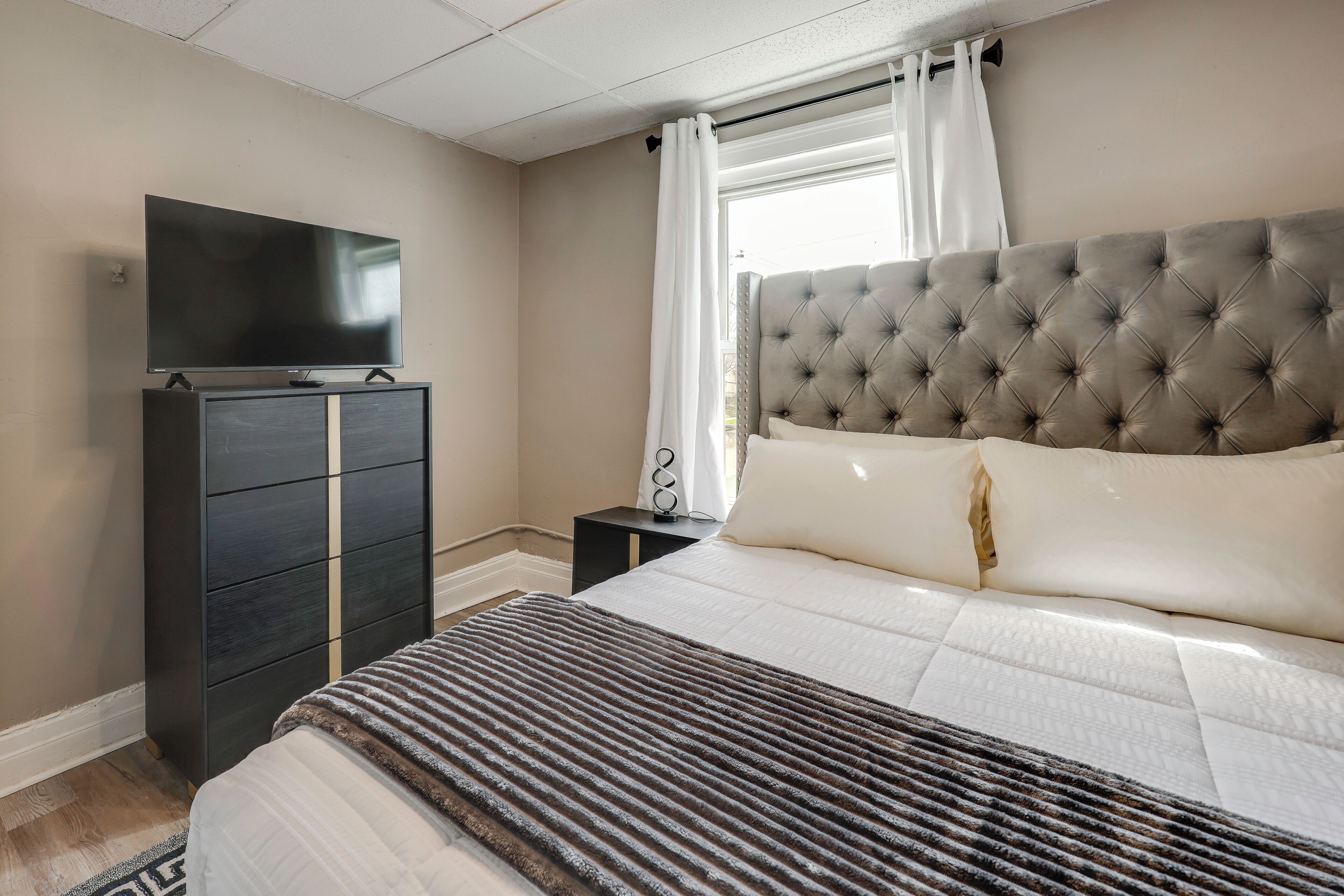 Une chambre à coucher avec un lit, une télévision, une commode et une fenêtre avec des rideaux.