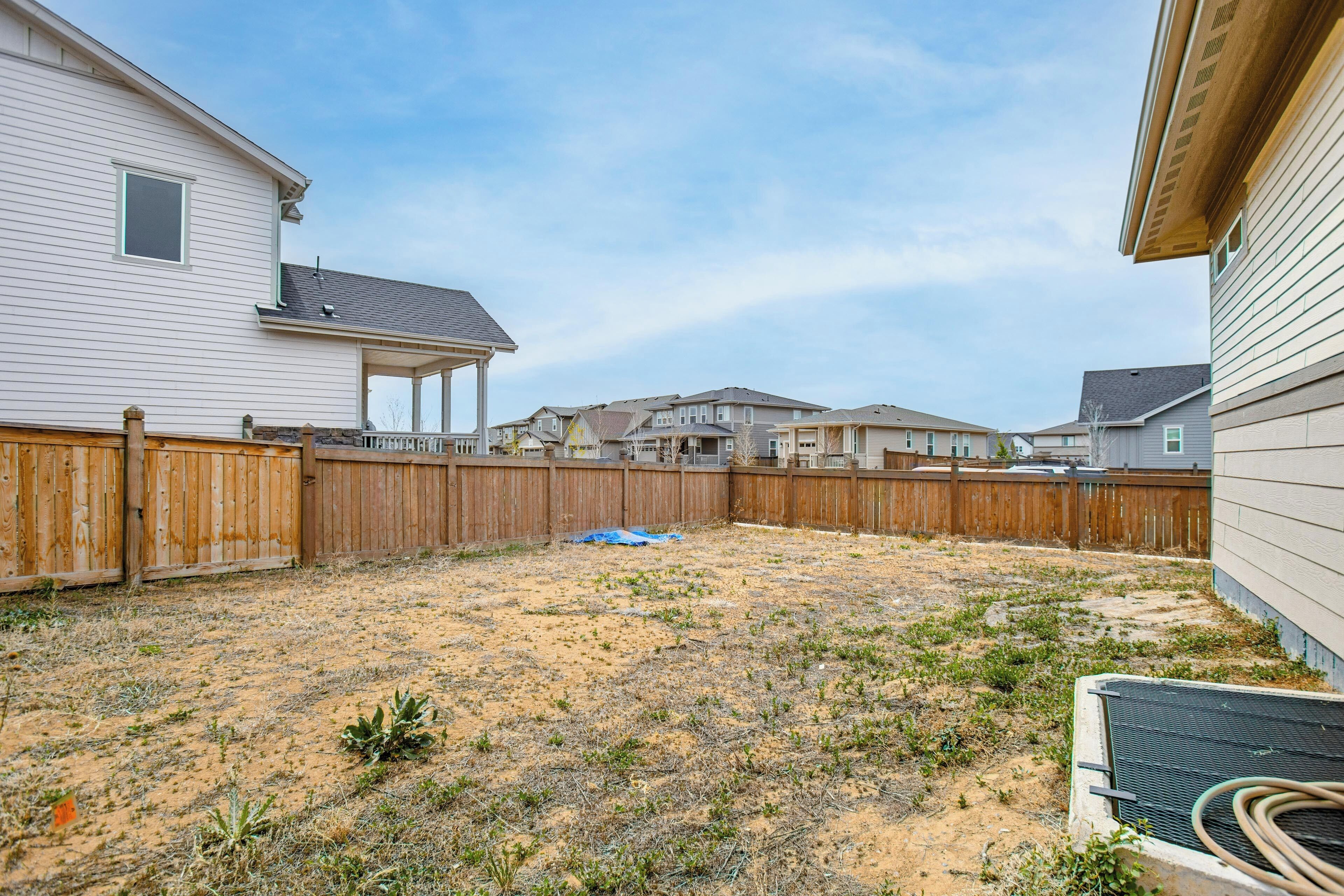 A backyard with a wooden fence, a covered patio area, and a sandy ground.