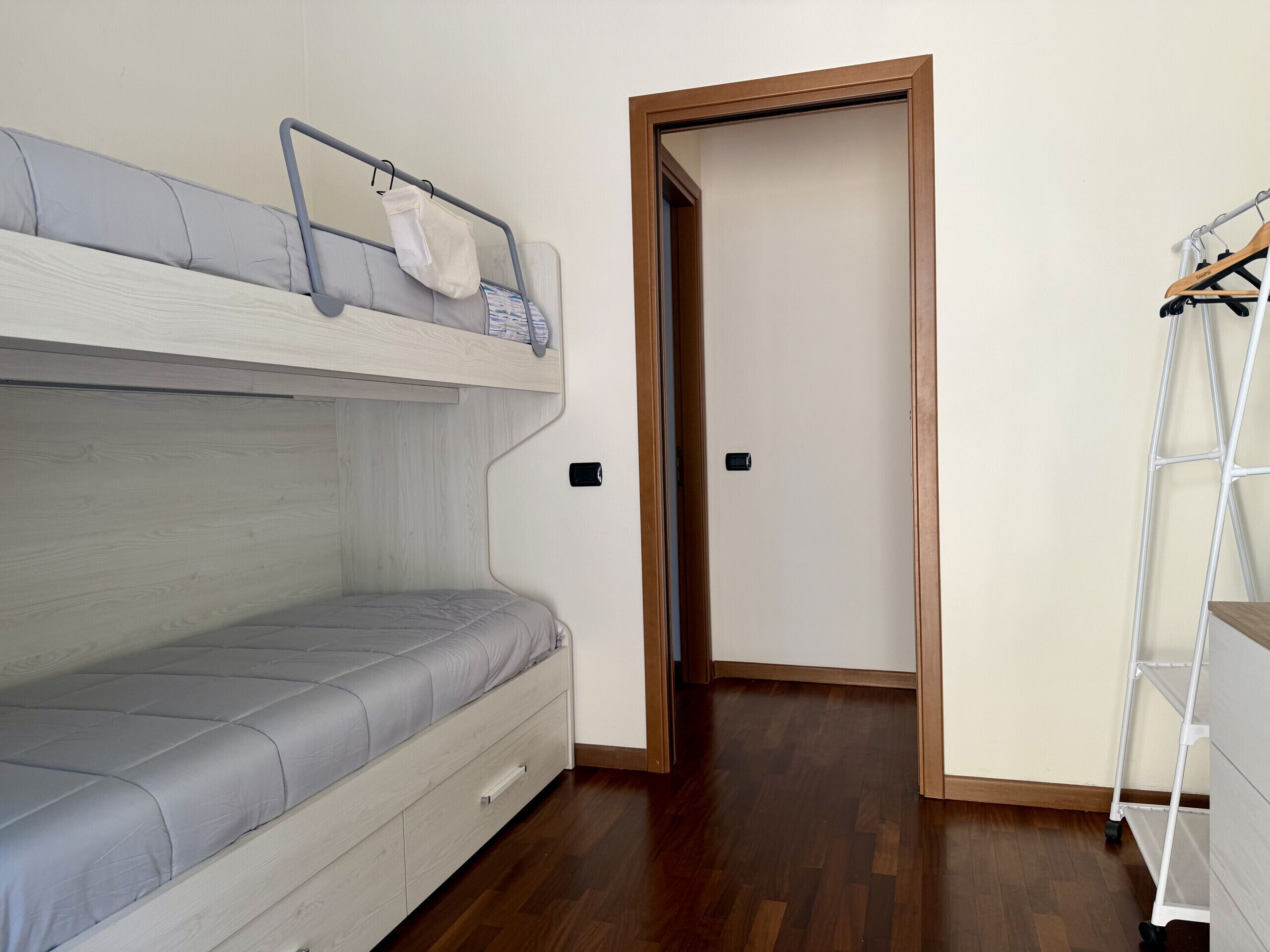 A room with a bunk bed, a wooden door, and a white metal shelf unit.