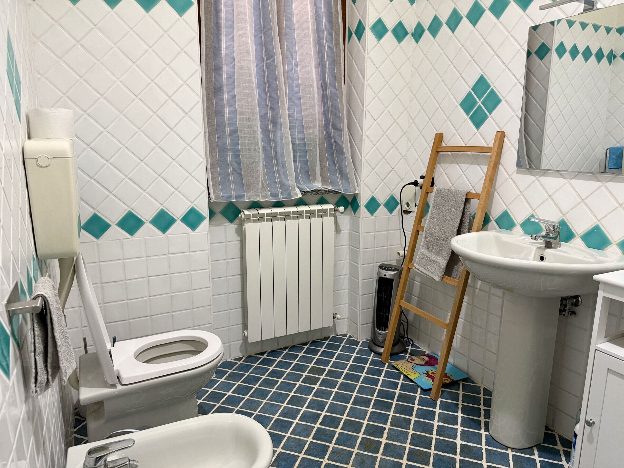 Et badeværelse med toilet, bidet, vask og en radiator.