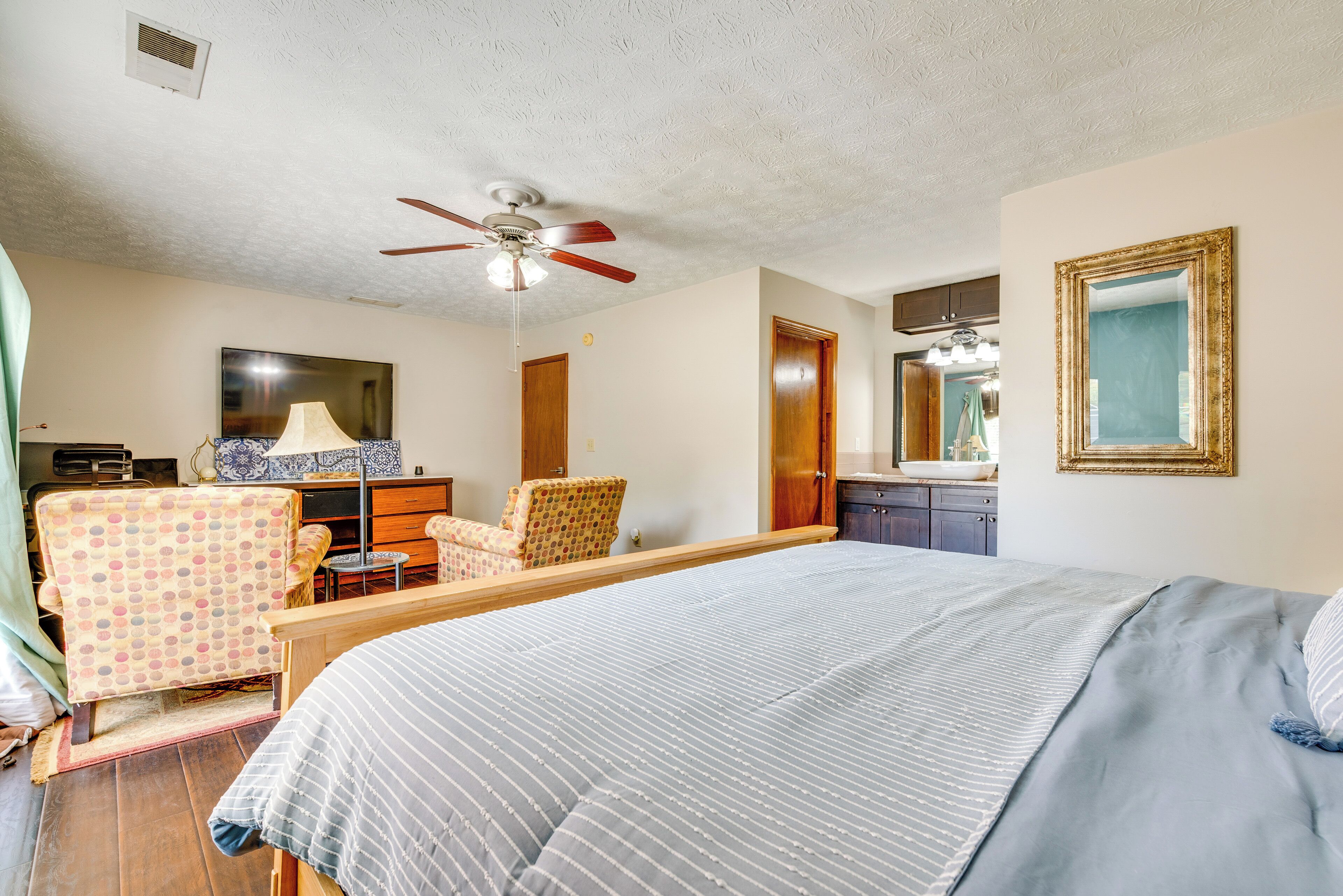 Une chambre à coucher comprenant un lit, un bureau, une chaise, un ventilateur de plafond, un miroir et une porte.