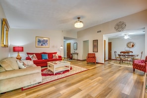 Un salón amplio con un sofá rojo, un sillón beige, una mesa de comedor con sillas y un ventilador de techo.