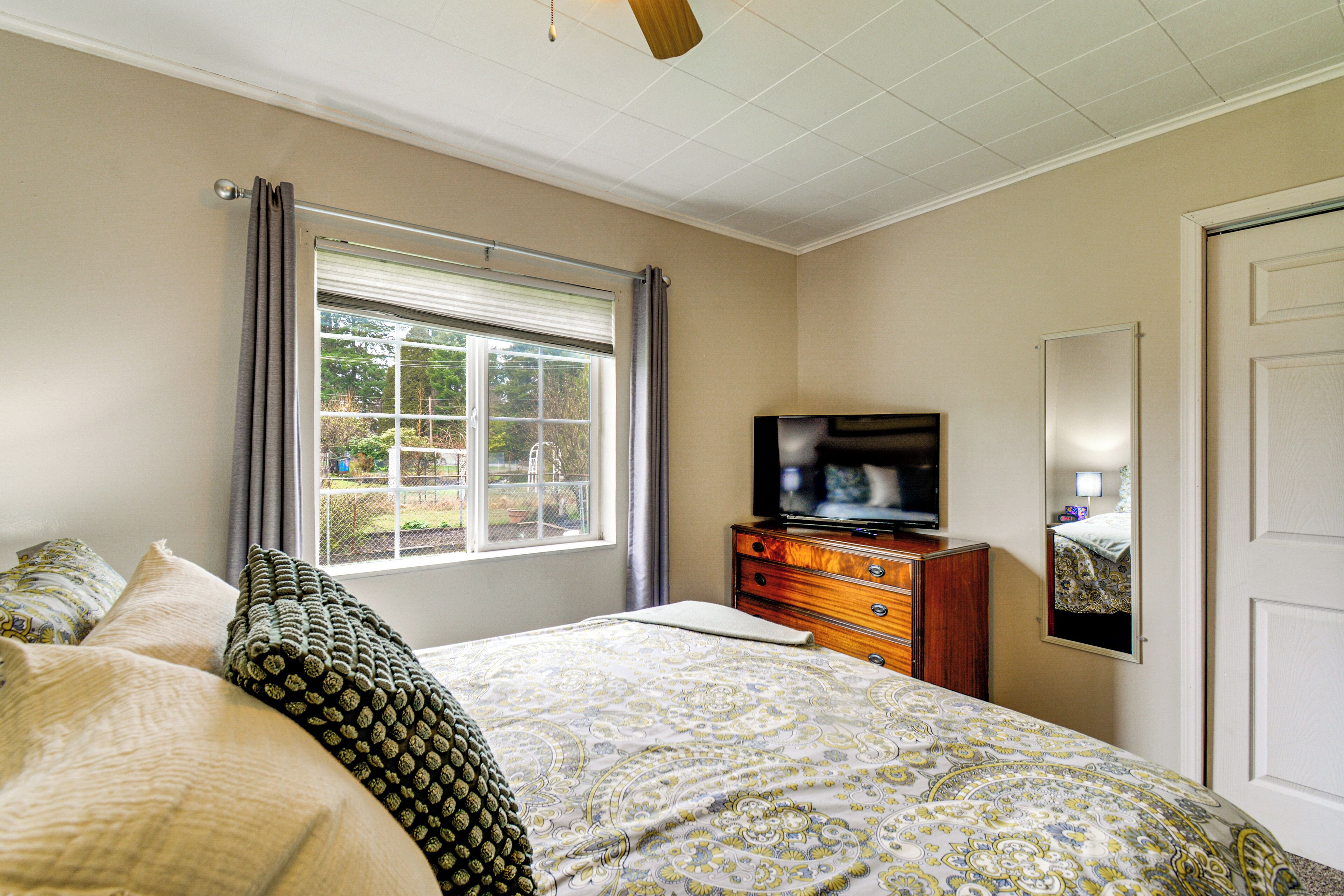 A bedroom with a bed, a dresser, a television, a window with curtains, and a door.