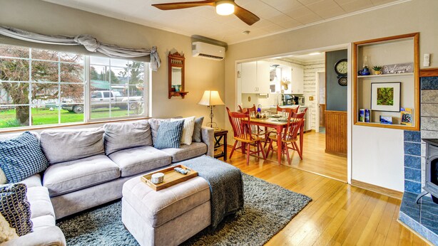 Una sala de estar con un sofá, reposapiés y una zona de comedor con sillas y una mesa.