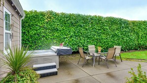 Un patio con un jacuzzi, sillas y una mesa, rodeado por un seto verde y frondoso.