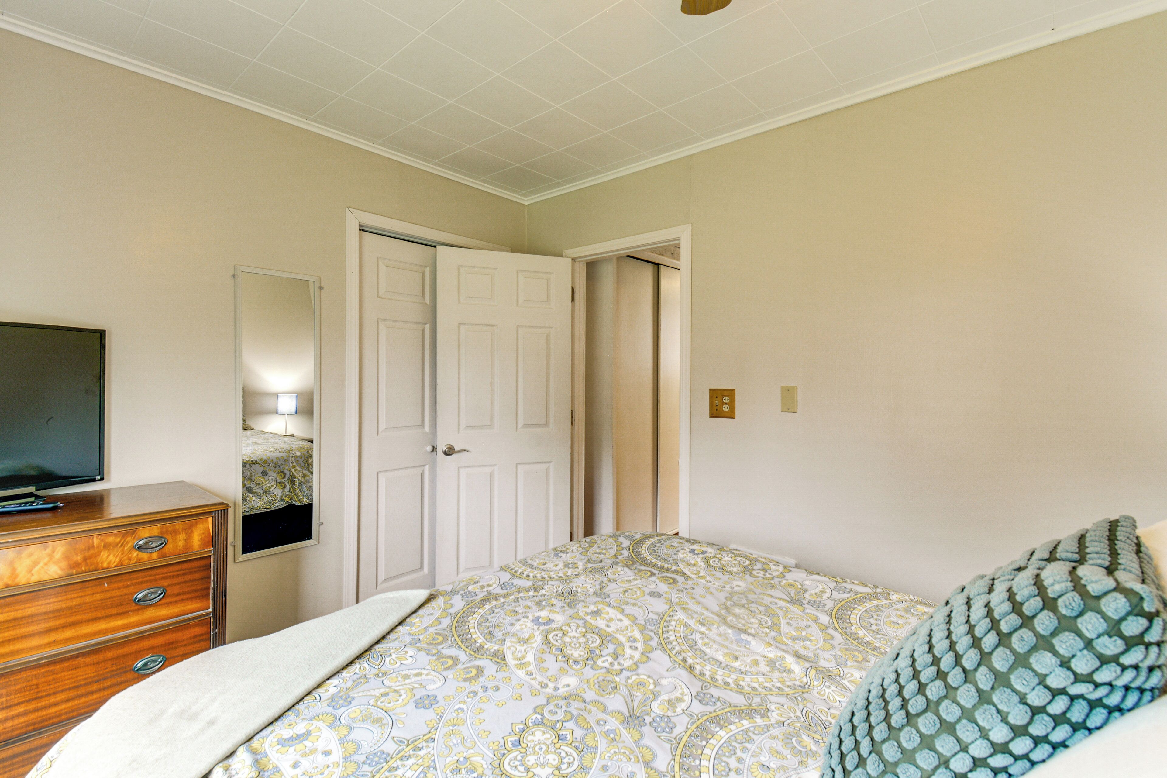 A bedroom with a bed, dresser, television, and a door leading to another room.