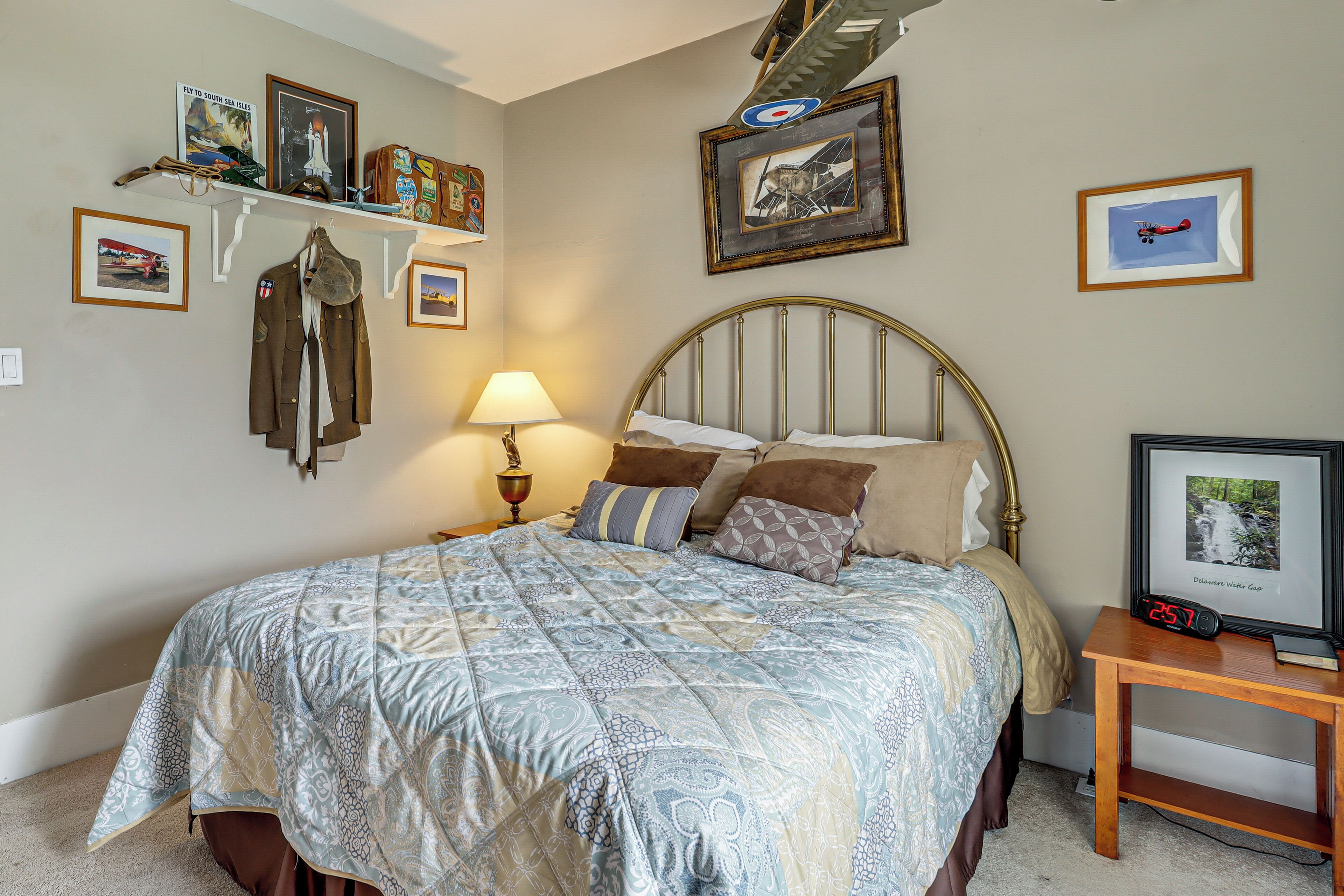 Un dormitorio con cama, mesita de noche con reloj, lámpara y cuadros en la pared.