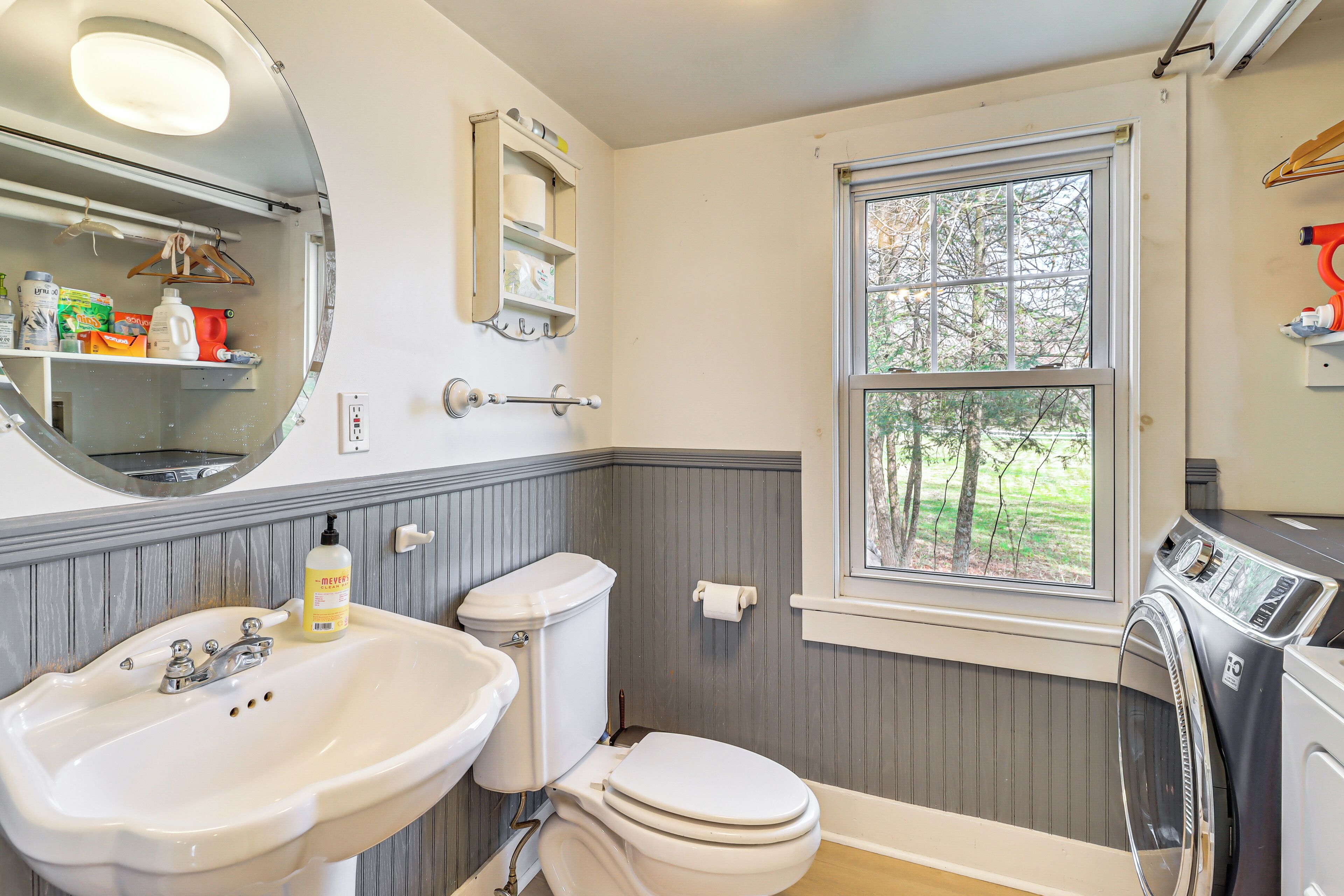A bathroom with a sink, toilet, window, and a washing machine.