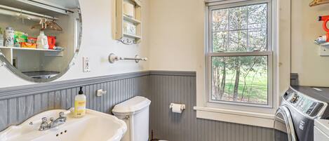 A bathroom with a sink, toilet, window, and a washing machine.