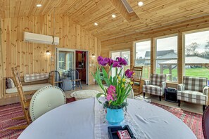 A wooden interior with a round table, chairs, a blue vase with flowers, and a view of the outside. - Private Lake, Hot Tub & Sauna: Poconos Retreat (Stroudsburg)