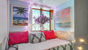 A bed with patterned bedding, a vase with flowers, and wall art including a beach scene and a sunset.