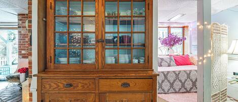 A wooden cabinet with glass doors, a brick wall, and a patterned sofa.