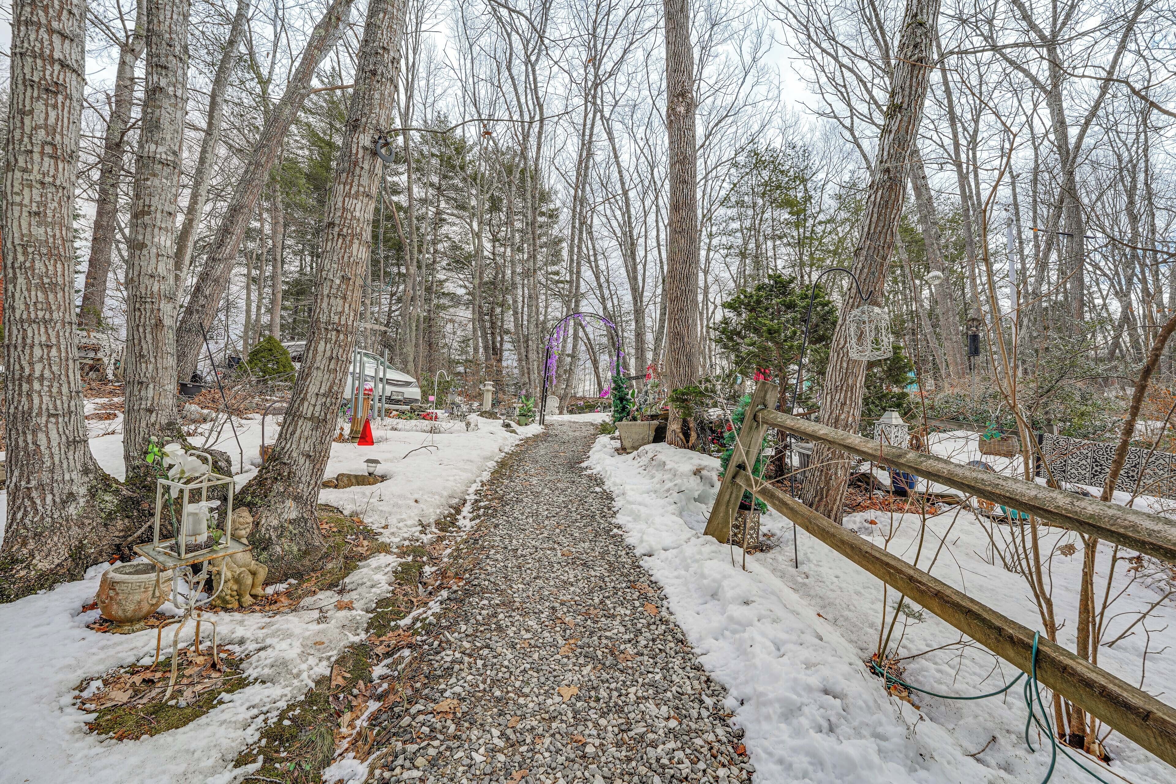 A snow-covered path in a wooded area with trees and a wooden fence.