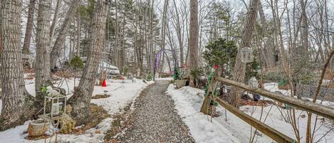 A snow-covered path in a wooded area with trees and a wooden fence.