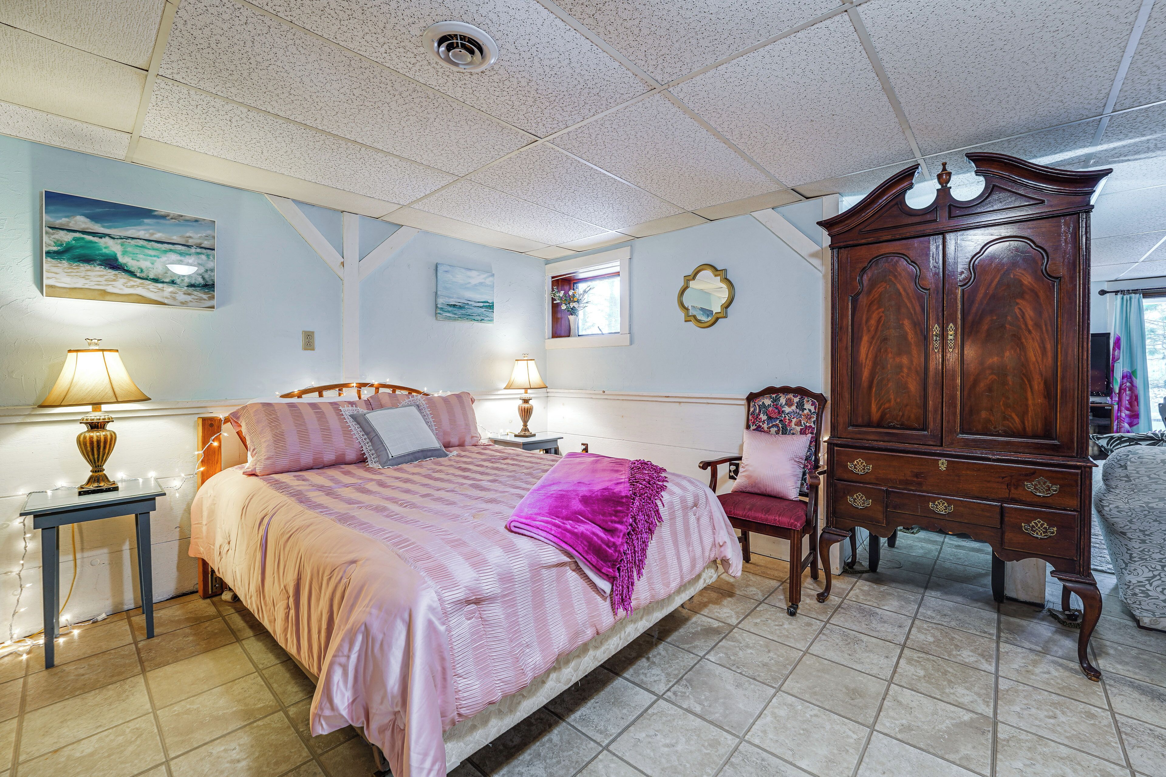 A bedroom with a bed, bedside tables, a dresser, a chair, and artwork on the walls.
