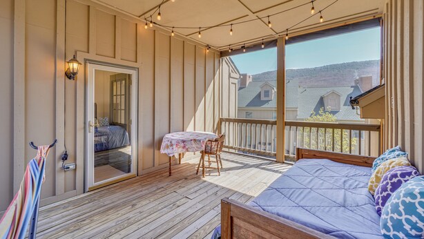 A room with a bed, a table, and a chair, a balcony with a railing, and a view of houses. - Pool Access! Amazing Mtn Retreat in Mercersburg (Mercersburg)