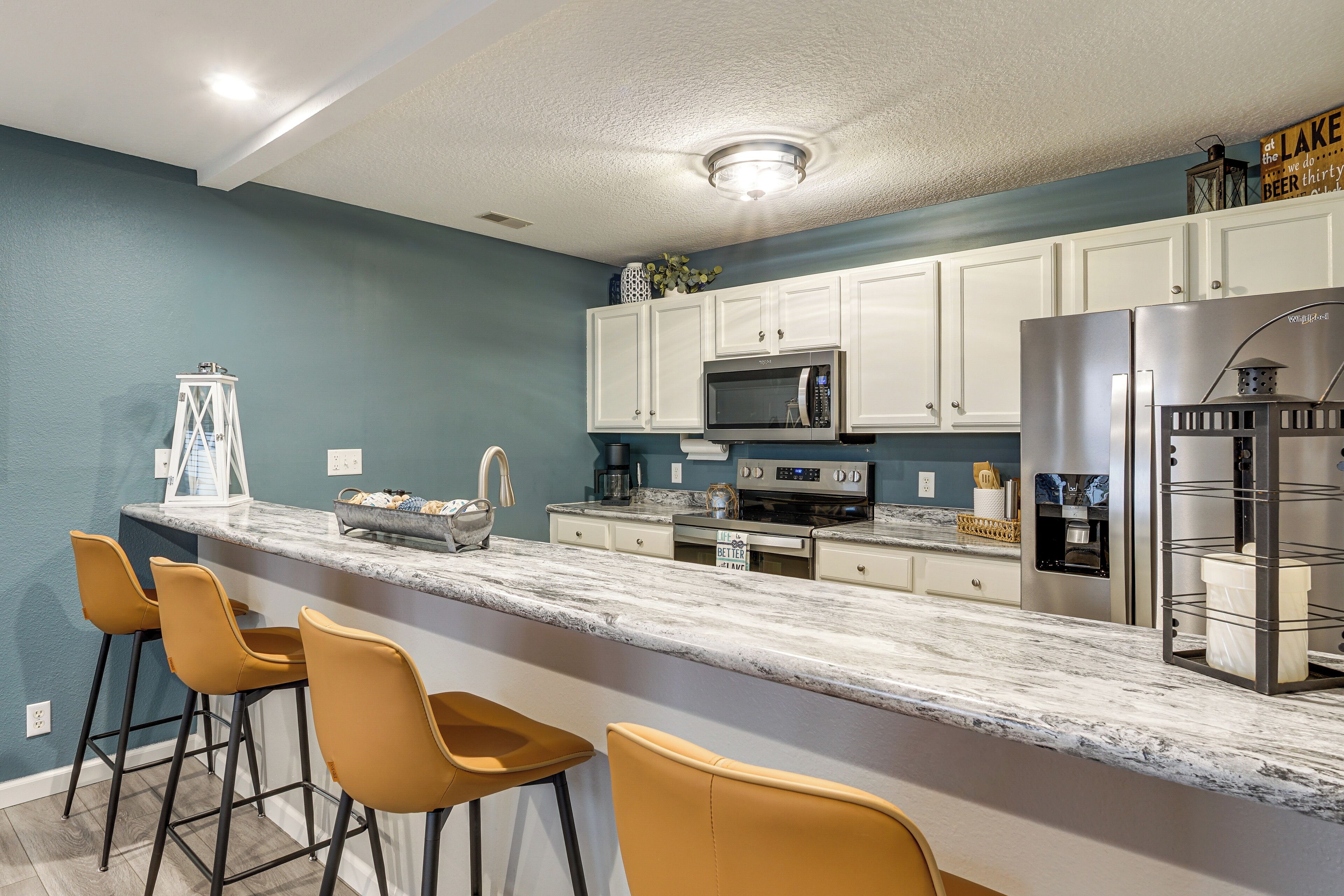 A modern kitchen with a marble countertop, white cabinets, and stainless steel appliances.