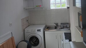 Ett litet kök med tvättmaskin, diskho och ett fönster.