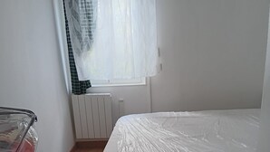 Ett sovrum med en säng, ett element, ett fönster med gardin och ett element som syns på väggen.