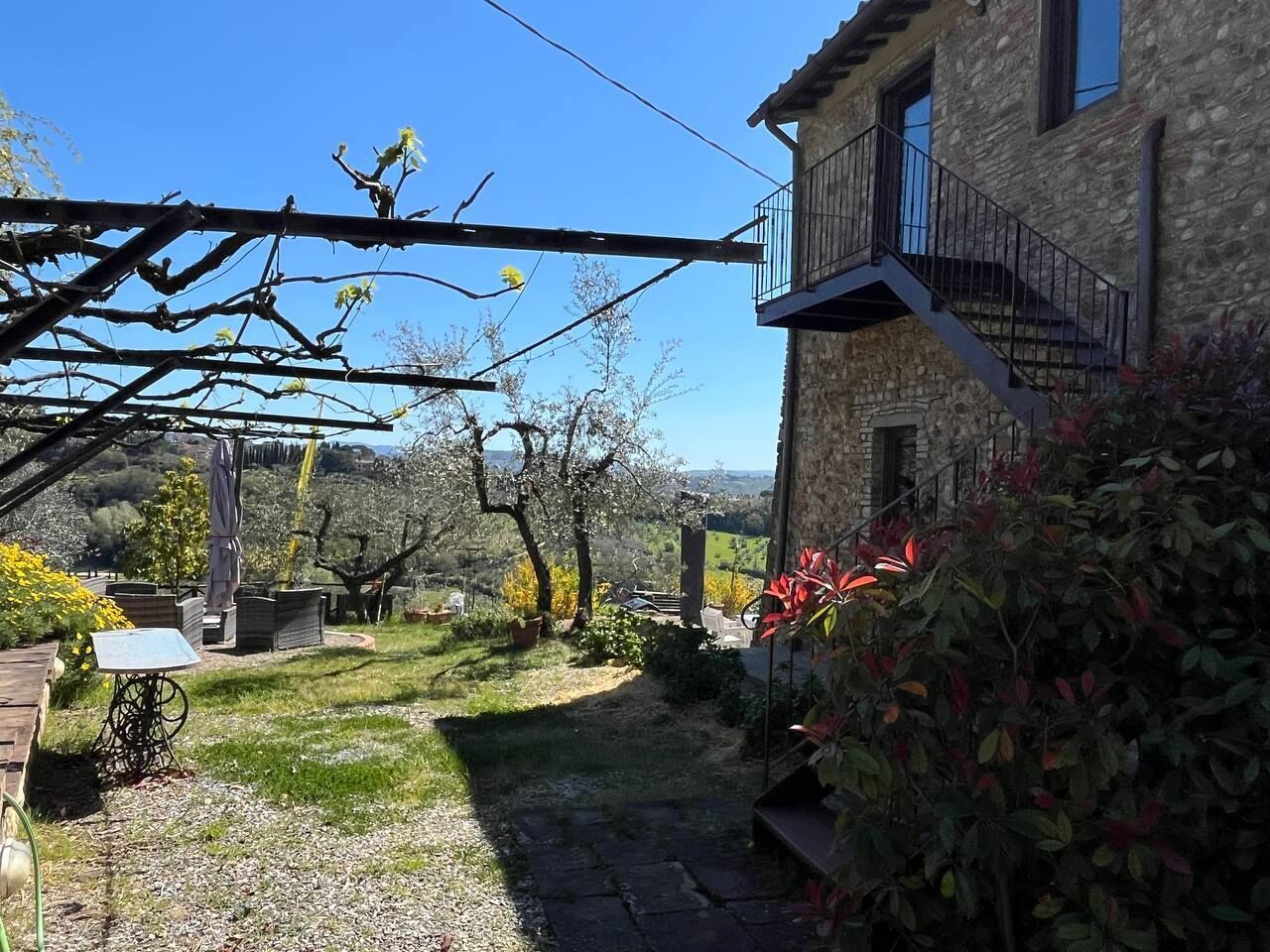 A stone building with a balcony, a garden with a table and chairs, and a view of the countryside.