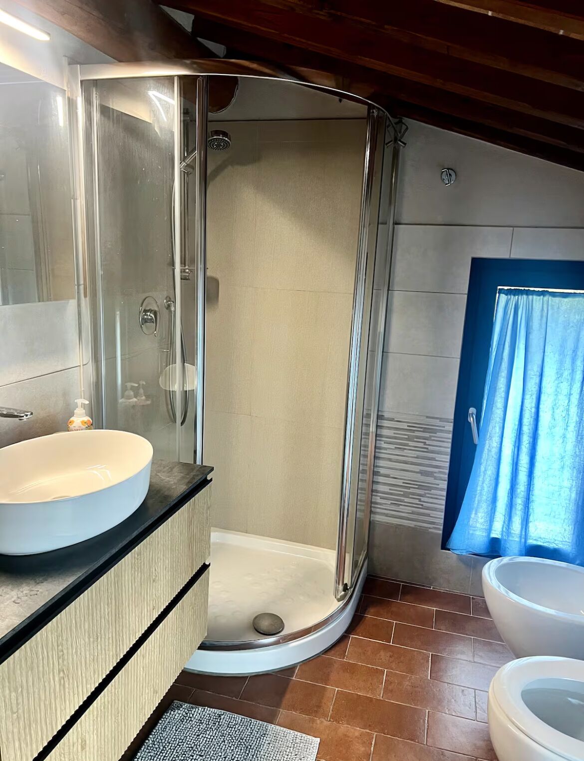 Casa de banho com chuveiro em cabine de vidro, lavatório branco e sanita.