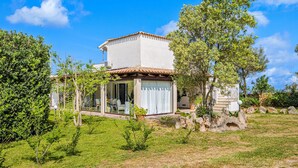 A house with a tiled roof, a glass door entrance, and a garden with grass and trees. - Holiday Home 'Villa Fortuna Con Vista Mare' with Sea View, Wi-Fi and Air Conditioning (Baja Sardinia)
