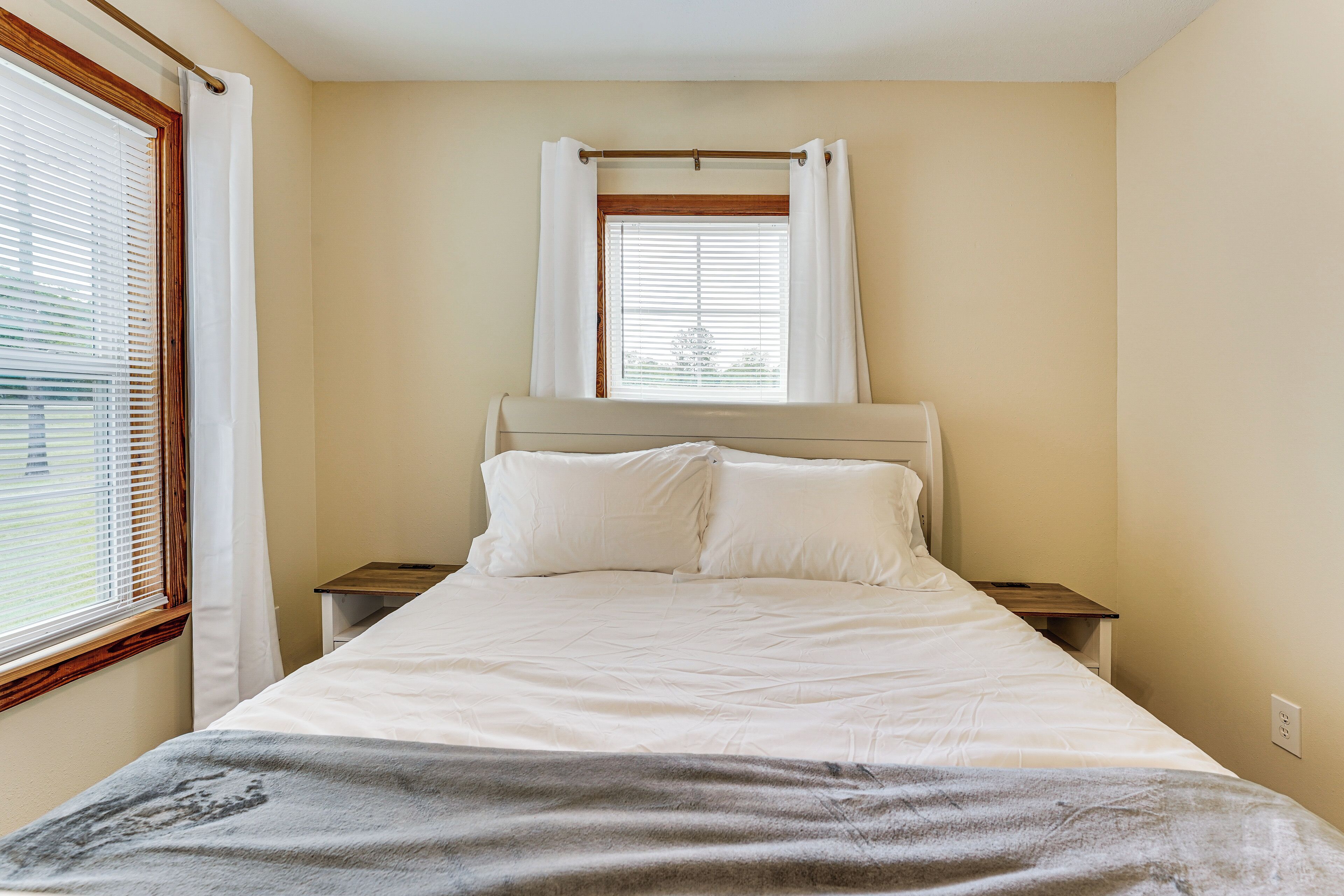 A bedroom with a bed, a window with blinds, a bedside table, and a headboard.