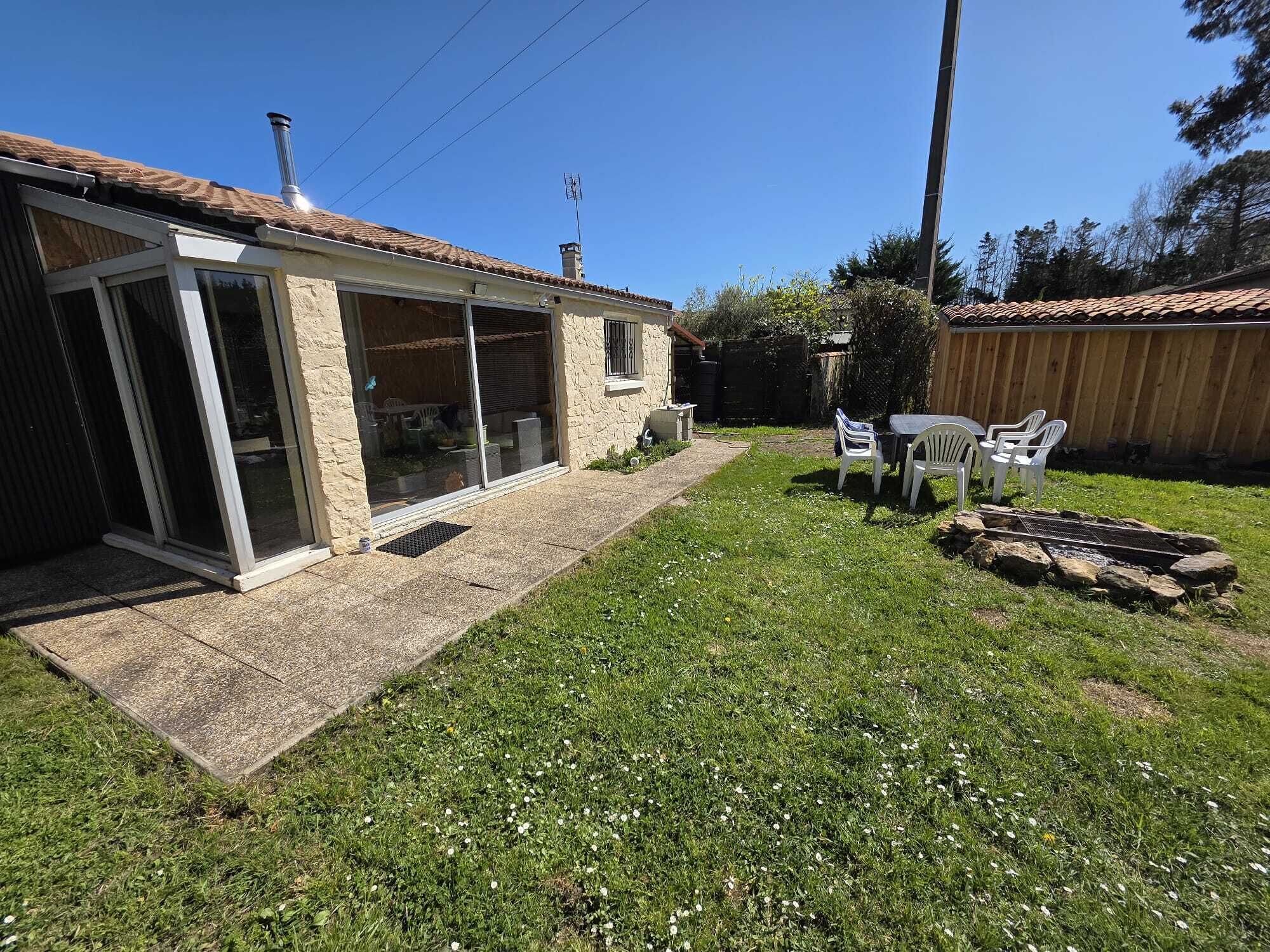 Une maison avec un patio, une cheminée en pierre et une cour arrière clôturée.