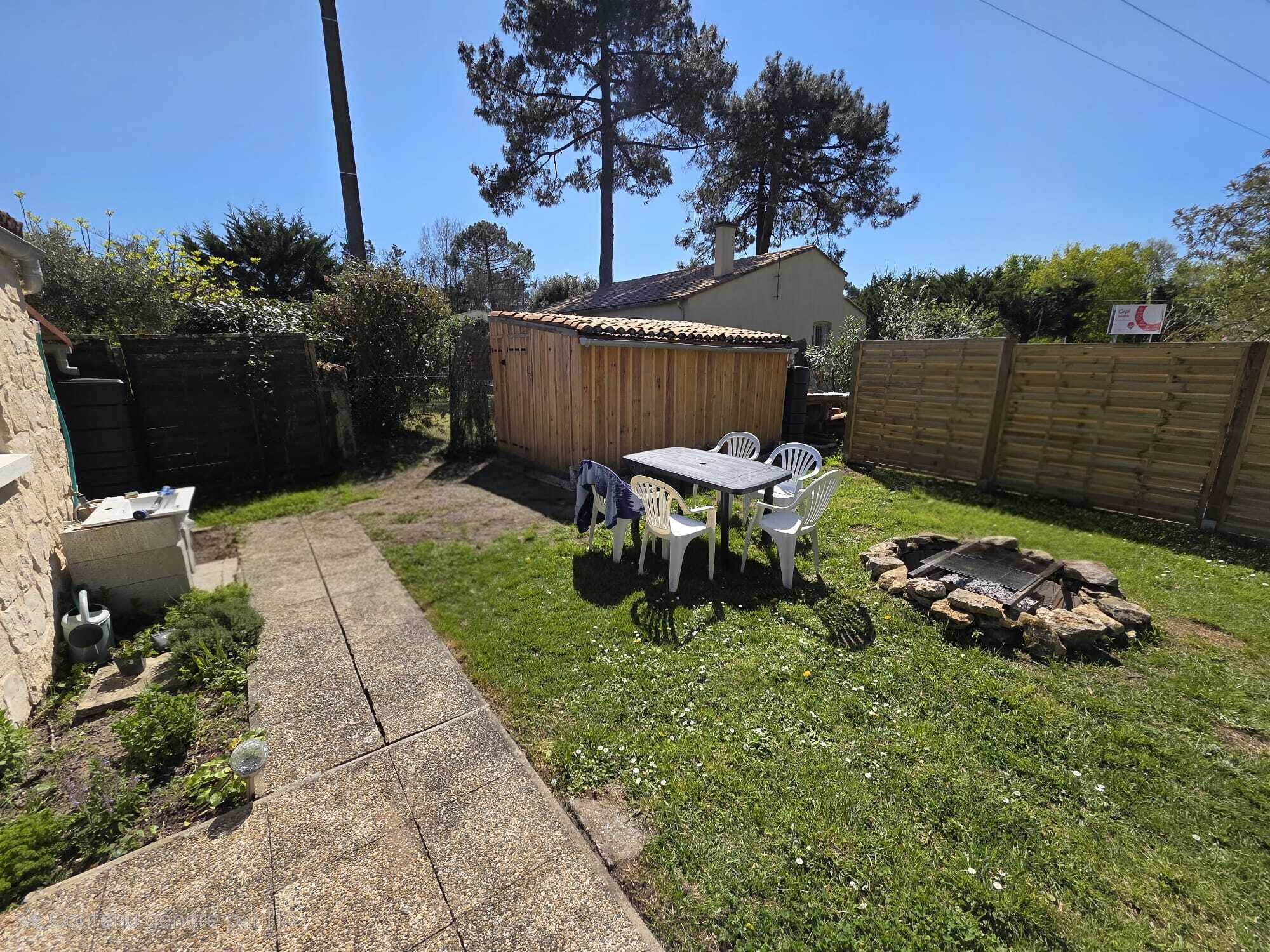 A backyard with a wooden shed, a concrete pathway, a table with chairs, and a fire pit.