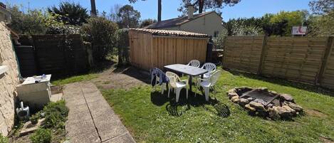 A backyard with a wooden shed, a concrete pathway, a table with chairs, and a fire pit.