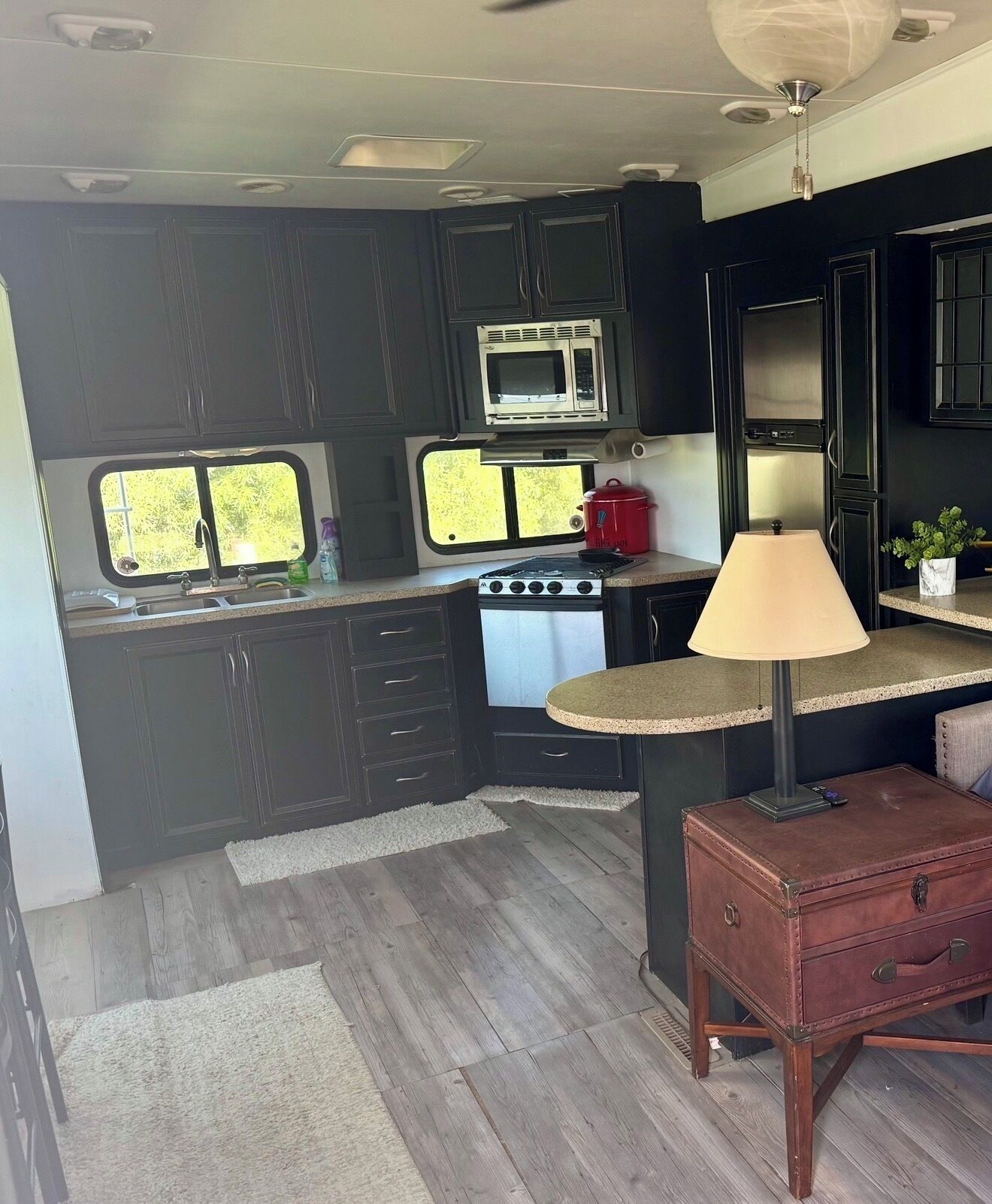 A compact kitchen with dark cabinetry, a microwave, a stove, a sink, and a small table with a lamp.