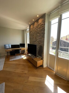 A modern living room with a stone accent wall, a flat-screen TV, a wooden entertainment unit, and large windows. - Villa Katerina - Luxury Apartment (Nice)