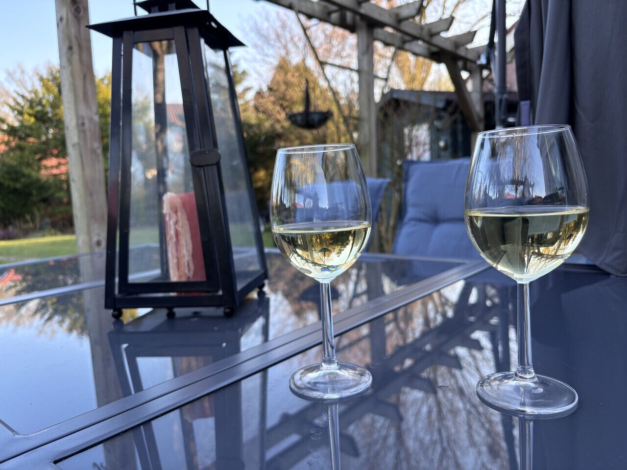 Two wine glasses on a glass table with a lantern and a view of trees.