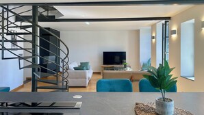 A modern living room with a spiral staircase, a flat-screen TV, and a dining area with a table and chairs. - Appartement du Châtel (Provins)