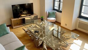 A modern living room with a glass coffee table, a flat-screen TV, a sofa, and a chair. - Appartement du Châtel (Provins)