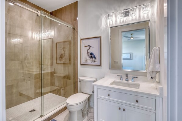 Un bagno moderno con doccia vetro, vaso, lavandino con specchio e un quadro incorniciato con un uccello.