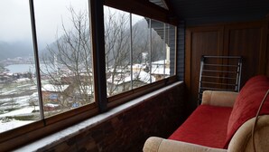 A room with a large window, a stone wall, a beige sofa with a red throw, and a metal drying rack. - Özkan Pansiyon (Caykara)