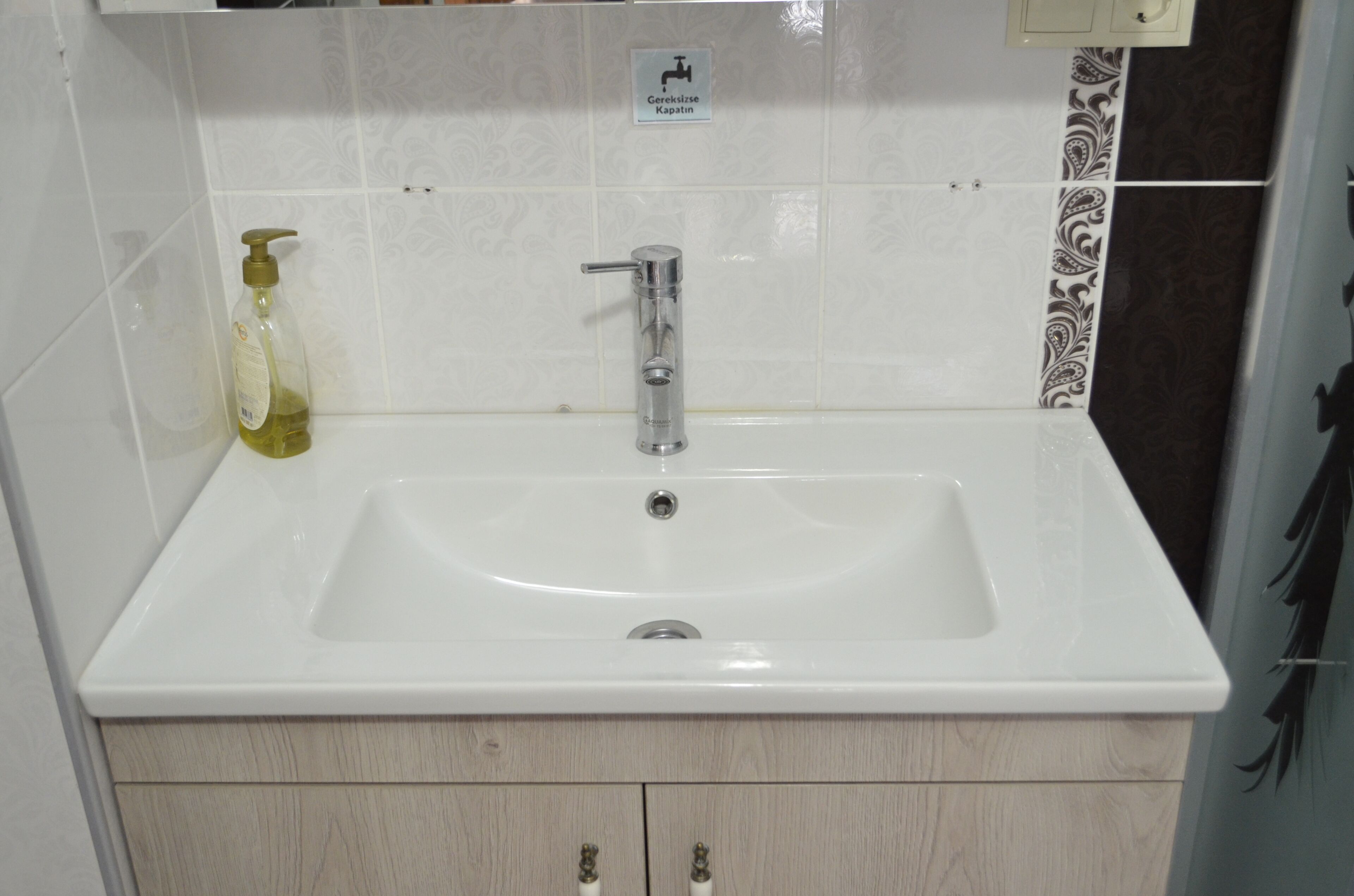 A bathroom with a white sink, a soap dispenser, and a sign indicating a towel rack.