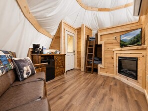 A cozy tented accommodation with a kitchenette, a fireplace, and a television.