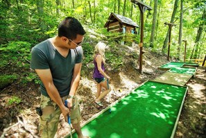 A person playing mini-golf in a wooded area with a small wooden structure in the background. - Glamping | Cozy Smoky Stay | Sleeps 4 - Cub House (Sevierville)