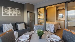 Ein modernes Hotelzimmer mit Essbereich, einer Couch, einem Bett und Blick durch eine Glastür.